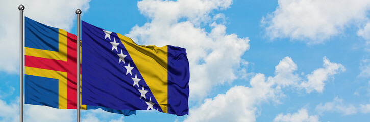 Aland Islands and Bosnia Herzegovina flag waving in the wind against white cloudy blue sky together. Diplomacy concept, international relations.