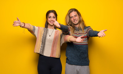 Hippie couple over yellow background presenting and inviting to come with hand - obrazy, fototapety, plakaty