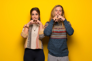 Hippie couple over yellow background showing a sign of silence gesture