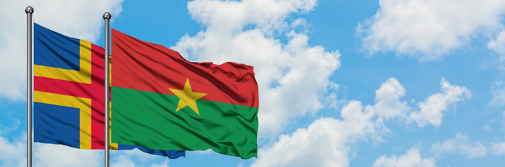 Fototapeta na wymiar Aland Islands and Burkina Faso flag waving in the wind against white cloudy blue sky together. Diplomacy concept, international relations.
