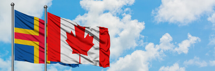 Aland Islands and Canada flag waving in the wind against white cloudy blue sky together. Diplomacy concept, international relations.