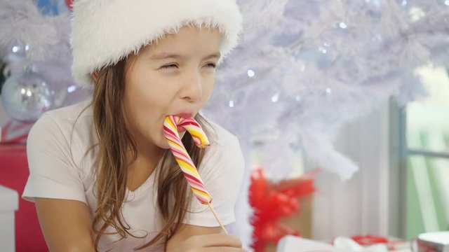 Pretty little girl is tasting a candycane, on Christmas morning, looking curious.