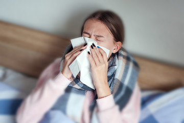 A sick girl with a headache sits under a blanket. Sick woman with seasonal infections, flu,...
