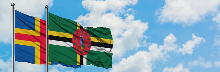 Aland Islands and Dominica flag waving in the wind against white cloudy blue sky together. Diplomacy concept, international relations.