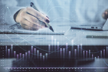 Double exposure of woman's hands making notes with forex graph hologram. Concept technical analysis.