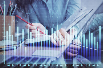 A woman hands writing information about stock market in notepad. Forex chart holograms in front. Concept of research. Multi exposure