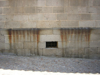 Small window in a stone wall, on a cobbled street in Avila, Spain