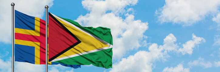 Aland Islands and Guyana flag waving in the wind against white cloudy blue sky together. Diplomacy concept, international relations.