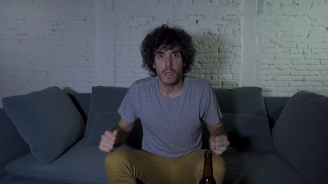 4k steady cam shot of lifestyle portrait of football fan watching soccer game on TV at home couch. Young mand screaming and celebrating goal or victory. In In sports, people and entertaiment.