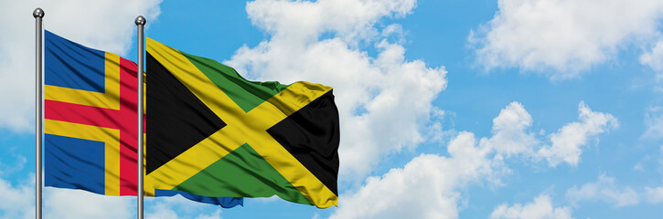 Aland Islands and Jamaica flag waving in the wind against white cloudy blue sky together. Diplomacy concept, international relations.
