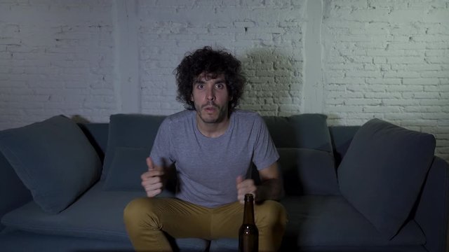 4k steady cam shot of lifestyle portrait of football fan watching soccer game on TV at home couch. Young mand screaming and celebrating goal or victory. In In sports, people and entertaiment.