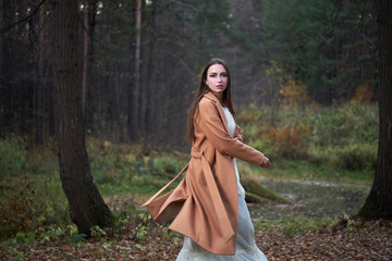 girl in a white dress and a brown coat in the autumn forest