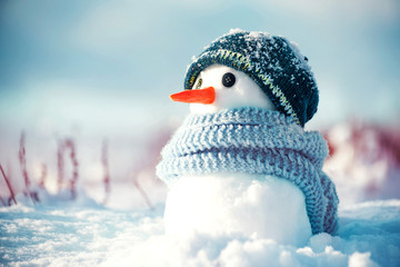 Little cute snowman in a knitted hat and scarf on snow on a sunny winter day. Christmas card - obrazy, fototapety, plakaty