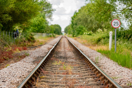 Detailed view of steel railway tracks taken from inside the parallel tracks, seen merging into the distance. A railway speed limit sign is also seen