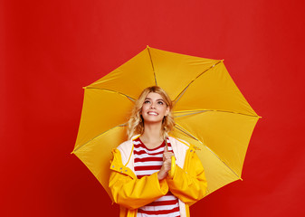 young happy emotional cheerful girl laughing and jumping with yellow umbrella   on colored red background.
