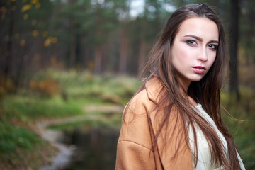 Naklejka premium girl in a white dress and a brown coat in the autumn forest