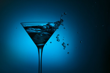 cocktail glass with blue alcoholic drink splashing out, close-up. 