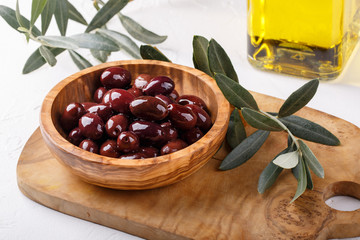 Whole black olives in wooden bowl on white table. Close-up.