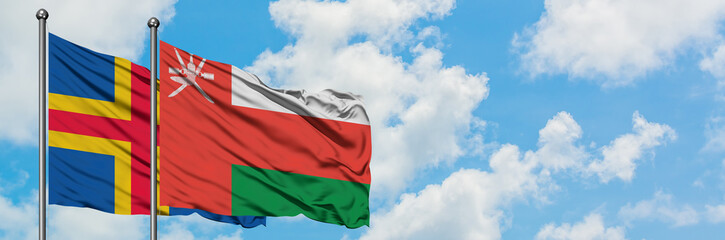 Aland Islands and Oman flag waving in the wind against white cloudy blue sky together. Diplomacy concept, international relations.