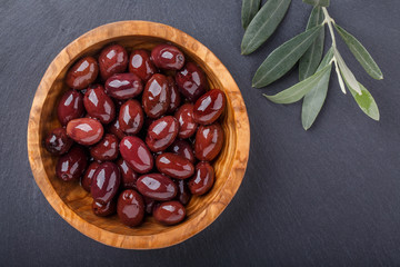 Whole black  olives in wooden bowl on black  background. Top view, close-up