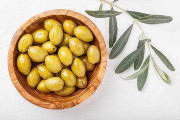 Whole green olives in wooden bowl on white background. Top view, close-up