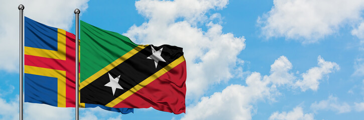 Aland Islands and Saint Kitts And Nevis flag waving in the wind against white cloudy blue sky together. Diplomacy concept, international relations.