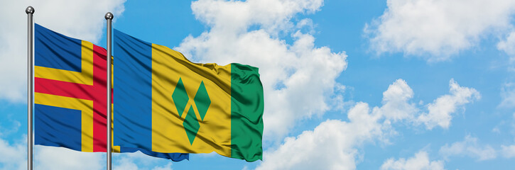Aland Islands and Saint Vincent And The Grenadines flag waving in the wind against white cloudy blue sky together. Diplomacy concept, international relations.