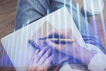 Double exposure of man doing notes of stock market with forex graph.