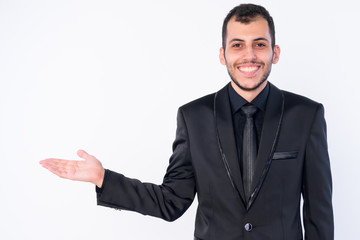 Portrait of happy young bearded Persian businessman in suit showing something