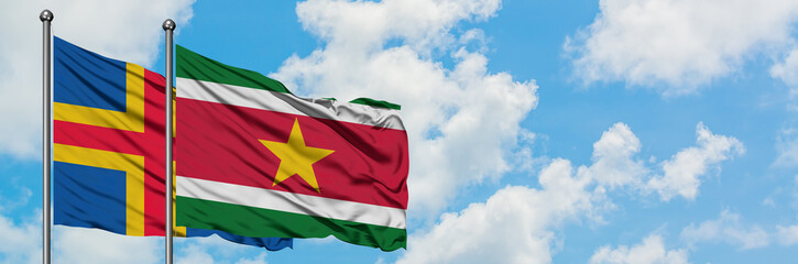 Fototapeta na wymiar Aland Islands and Suriname flag waving in the wind against white cloudy blue sky together. Diplomacy concept, international relations.