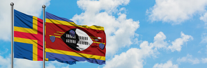 Aland Islands and Swaziland flag waving in the wind against white cloudy blue sky together. Diplomacy concept, international relations.