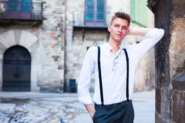 Fototapeta na wymiar young European guy in shirt and trousers with suspenders walking around city