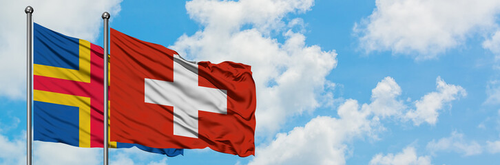 Aland Islands and Switzerland flag waving in the wind against white cloudy blue sky together. Diplomacy concept, international relations.