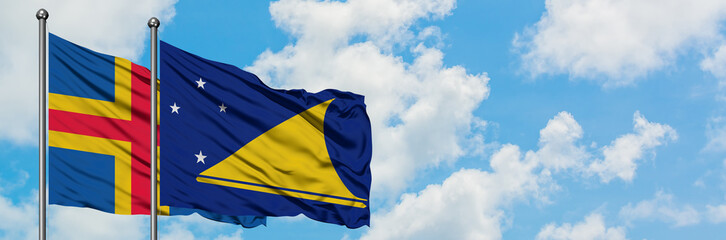 Aland Islands and Tokelau flag waving in the wind against white cloudy blue sky together. Diplomacy concept, international relations.