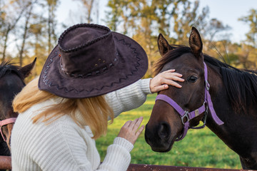Obraz premium Woman with cowboy hat is stroking her young horse at farm