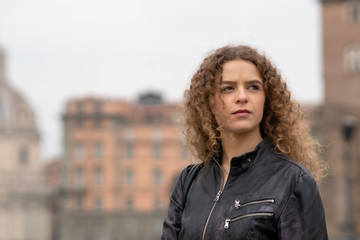 Fototapeta premium Young woman with curly hair outdoors in Rome, with a black leather jacket. Copy space.