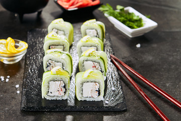 Uramaki sushi rolls with cream cheese, snow crab, cucumber, flying fish caviar, mayonnaise, lemon and nori closeup. Macro shot of seafood sushi on dark blurred background
