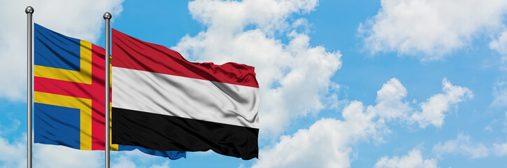 Aland Islands and Yemen flag waving in the wind against white cloudy blue sky together. Diplomacy concept, international relations.