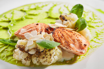 Salmon steak on plate closeup. Red fish piece with green pea puree and cauliflower. Salmon with creamy sauce and vegetables isolated on white background. Restaurant tasty dish, cooked healthy meal