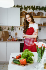 young housewife in the kitchen in an apron will cook vegetables