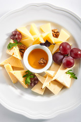 Cheese Platter with Honey, Nuts and Grapes on White Restaurant Plate