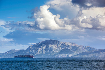 Fototapeta na wymiar Barco mercante surcando el Estrecho de Gibraltar con la montaña Jebel Musa (Africa) al fondo.