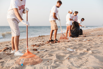 Image of caucasian volunteers cleaning beach from plastic with trash bags
