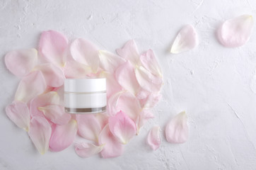 Top view of glass jar and pink delicate petals on the white surface.Empty space.Concept of natural cosmetics for beauty treatments