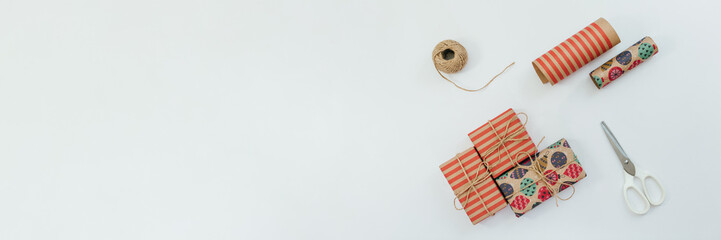 Photo of three multicolored gift boxes, scissor, wrapping kraft paper and jute ribbon. Preparation...