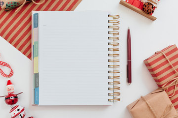 Photo of notebook with empty space for text. Plans for 2020 year. Near diary burgundy pen, wrapped kraft gift boxes and red fir toys. White background. Merry Christmas and Happy New Year concept.