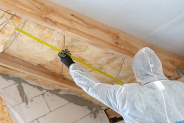 Professional builder man installing thermal insulation layer with fiberglass wool under the roof