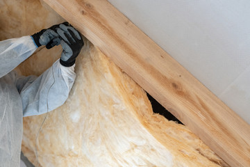Professional worker man installing thermal insulation layer with fiberglass wool under the roof