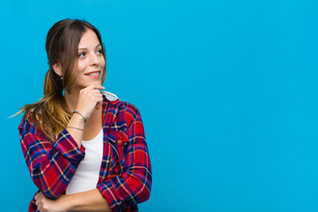 young pretty woman smiling with a happy, confident expression with hand on chin, wondering and...