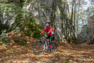 Fototapeta na wymiar nice senior woman riding her electric mountain bike in the autumnal atmosphere in the Hells Holes of the Swabian Alb near the city of Urach, Baden Wuerttemberg, Germany